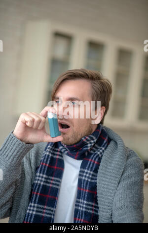 Blauäugiger junger Mann in Asthma Inhalator verwenden Stockfoto