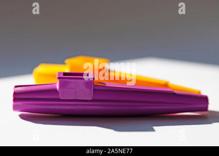 Ein lila und gelb Musikinstrument ist auf einer sonnigen Fensterbank, Kazoo entfernt Stockfoto