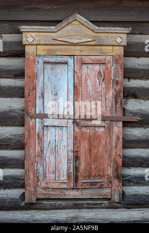 Geschlossen alte Fensterläden aus Holz Russischen Haus. Die Farbe abgeblättert und abgezogen. Bügeleisen Schraube. Blaue, rote und gelbe Farbe. Vertikale Stockfoto