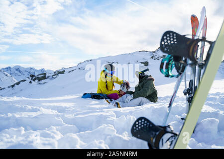 Bild von Ski, Snowboard, Ski Stöcke auf dem Hintergrund von zwei Touristen mit Thermoskanne in der Hand auf Schnee Resort am Nachmittag Stockfoto