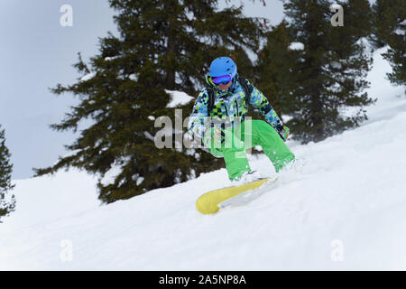 Männliche snowboarder Reiten am Berghang auf Hintergrund der Bäume am Nachmittag Stockfoto