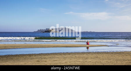 Ansicht der Frau mit Hut und rotes Hemd allein am Strand sitzen und starrte die westlichen Pazifischen Ozean in der Nähe von Tofino auf Vancouver Island Stockfoto