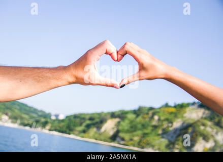 Männliche und weibliche Hände Gestaltung einer Liebe hand mit unscharfen Hintergrund des Berges und des Meeres Stockfoto