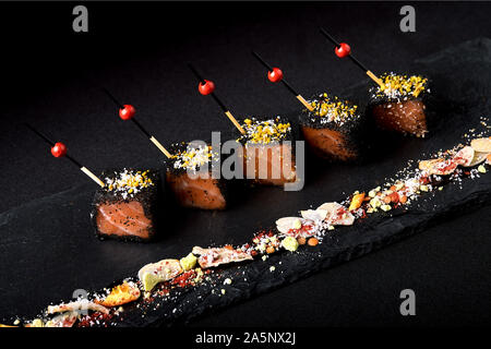 Gebeizter Lachs in Scheiben geschnitten in Schwarz, mit Paniermehl Spieße auf eine schwarze Platte gelegt. Fusion Food Konzept, Low Key, copy Space Stockfoto