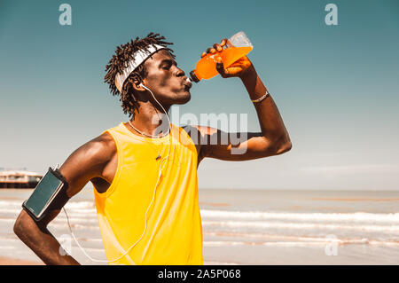 Schwarzer Läufer, der im Sommer am Strand trinkende Energydrinks ausruhen kann Stockfoto