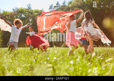 Gruppe von Kindern läuft und Tänze mit Handtüchern auf einer Wiese im Sommer Stockfoto