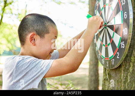 Asian Boy mit Dart, Dart spielen vor eine Dartscheibe Stockfoto