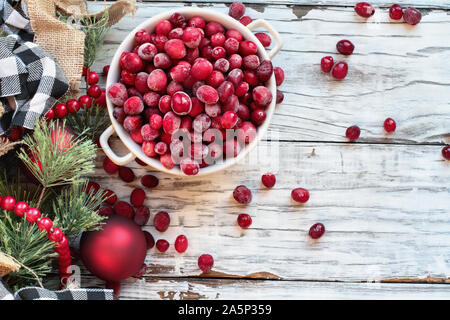 Gefrorene Cranberries in einer Schüssel über einem weißen Holz Tisch Hintergrund mit Weihnachtsschmuck. Ansicht von oben. Stockfoto