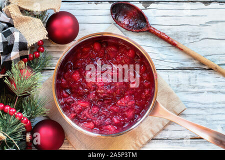 Sauce pan von Cranberry relsih über einem weißen Holz Tisch Hintergrund mit unordentlichen Holzlöffel und Weihnachtsschmuck. Ansicht von oben. Stockfoto