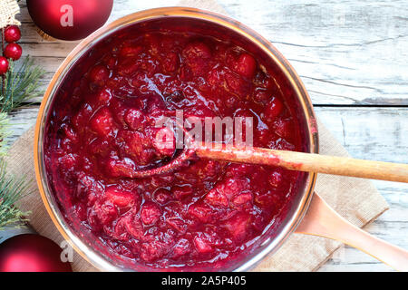 Sauce pan von Cranberry relsih über einem weißen Holz Tisch Hintergrund mit unordentlichen Holzlöffel und Weihnachtsschmuck. Ansicht von oben. Stockfoto