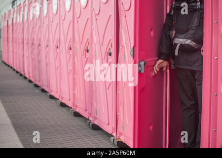 Ein Mann, der in einer sehr langen Reihe von Rosa mobile Toiletten. Stockfoto