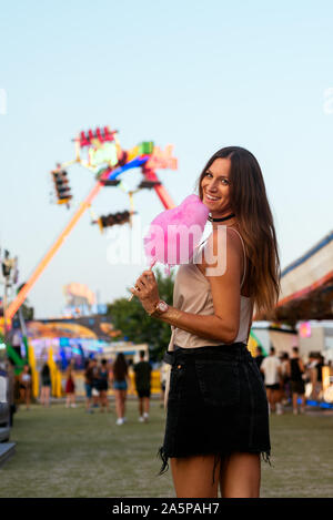 Junge Frau lächelnd in die Kamera auf einem Jahrmarkt mit einer Süßigkeit Baumwolle Stockfoto