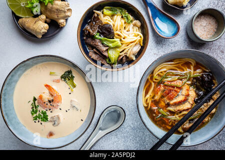 Satz serviert asiatische Suppen auf grauem Hintergrund der Ansicht von oben. Tom Yum Suppe, Aal Fischsuppe und Ramen Noodle Soup Stockfoto