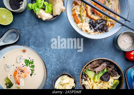 Satz serviert asiatische Suppen auf dunkelblauem Hintergrund der Ansicht von oben. Tom Yum Suppe, Aal Fischsuppe und Ramen Noodle Soup Stockfoto