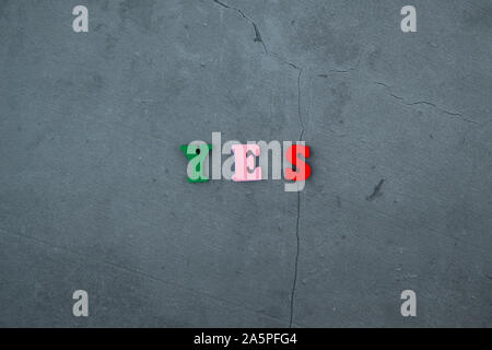 Die bunte Ja Wort ist aus Holz Buchstaben auf einem grau verputzte Wand Hintergrund gemacht Stockfoto