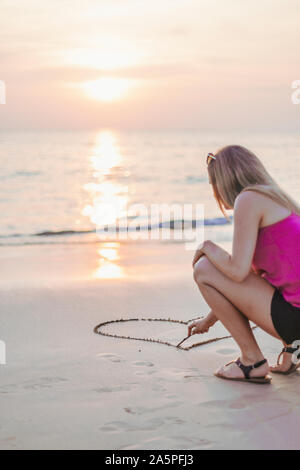 Junge Frau Zeichnung Herzform auf Sand Stockfoto