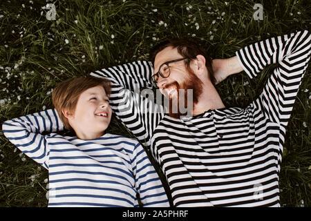 Vater und Sohn tragen ähnliche abgestreift Shirts liegen auf Gras Stockfoto