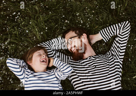 Vater und Sohn tragen ähnliche abgestreift Shirts liegen auf Gras Stockfoto