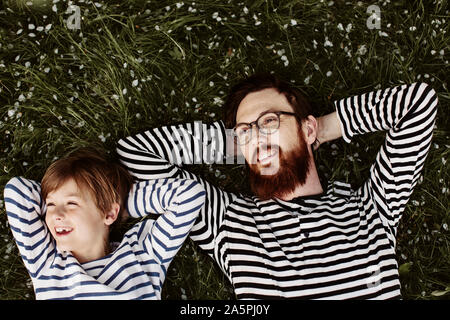 Vater und Sohn tragen ähnliche abgestreift Shirts liegen auf Gras Stockfoto