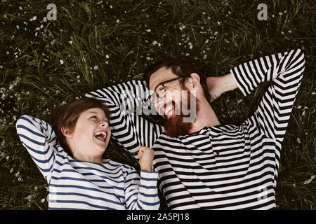 Vater und Sohn tragen ähnliche abgestreift Shirts liegen auf Gras Stockfoto