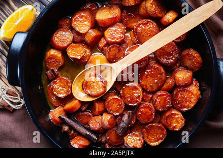 Kandierte Yamswurzeln, Süßkartoffeln zubereitet mit Orangensaft, Zimt, brauner Zucker und Butter in einem schwarzen Keramik Teller, Ansicht von oben, Makro, flatlay Stockfoto