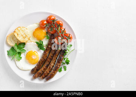 Gebratene Eier, Würstchen und Kirschtomaten auf die Platte über der weißen Stein mit freiem Text Raum Platz. Ansicht von oben, flach Stockfoto