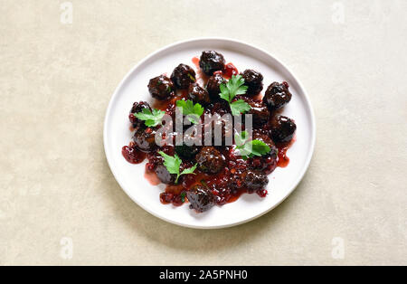 Frikadellen mit Preiselbeersoße auf weißen Platte über Licht Stein Hintergrund. Geschmorte Hackfleischbällchen in süßen Beeren-Sauce. Stockfoto
