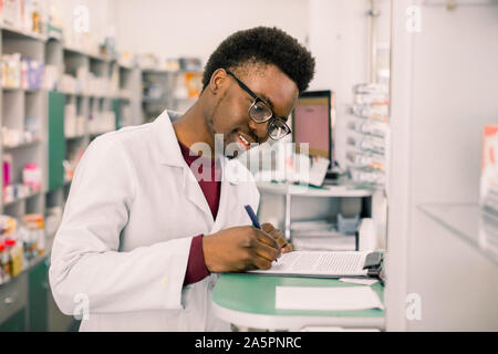 Portrait Of Happy African American Apotheker schreiben Rezept am Arbeitsplatz in modernen Pharmazie Stockfoto