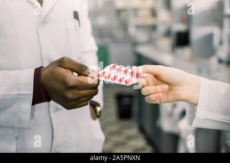 Männliche und weibliche Apotheken oder Ärzte in der Apotheke. In der Apotheke Willkommen. Zugeschnittenes Bild der Hände von Apotheken oder Ärzte holding Blister rot Stockfoto