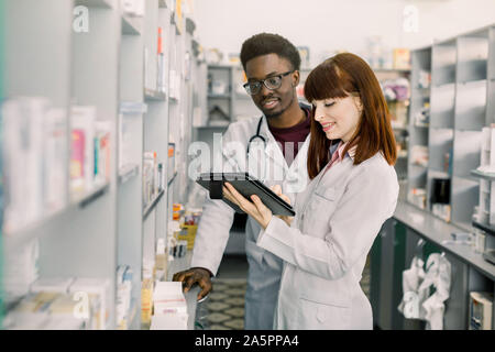 Zuversichtlich, dass männliche und weibliche Apotheker in der Apotheke. Weibliche Apotheker sprechen mit ihrer Kollegin über die Attribute und die Nebenwirkungen einer Medizin oder Stockfoto