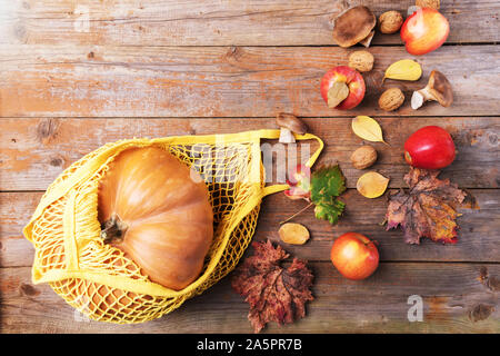 Herbst Kürbis in einem Gitter Baumwolle eco Beutel mit Äpfeln, cardoncelli Pilze, Nüsse, Blätter auf alten hölzernen Brettern. Herbst shopping, Ernte, Null Abfall Stockfoto