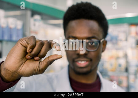 Junge lächelnde Afrikanisch-amerikanischen Arzt Apotheker Mann, weiße Tablette Pille in der Hand, close-up. Konzentrieren Sie sich auf die Hand Stockfoto