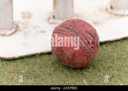 Eine Nahaufnahme von einem alten Brunnen verwendet Red cricket Ball auf einem Rasenplatz neben White Metal Wickets Stockfoto