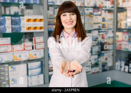 Freundliche Apotheker, Chemiker Frau im weißen Kittel in Apotheke Apotheke und halten in ihren Händen viele bunte Pillen Stockfoto