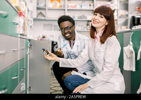 Seitenansicht von zwei engagierten Apothekern, afrikanischer Mann und kaukasische Frau, auf der Suche nach den besten Medizin beim zusammen in einer Gemeinschaft Apotheke arbeiten Stockfoto