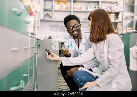 Seitenansicht von zwei engagierten Apothekern, afrikanischer Mann und kaukasische Frau, auf der Suche nach den besten Medizin beim zusammen in einer Gemeinschaft Apotheke arbeiten Stockfoto