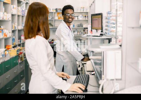 Weibliche und männliche Apotheker in der modernen Apotheke, an einander suchen, während der Arbeit am Computer Stockfoto