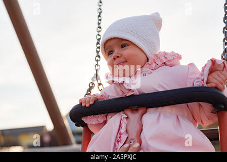 Adorable Baby Mädchen mit grossen schönen Augen und einem beanie Spaß auf einer Schaukel Stockfoto