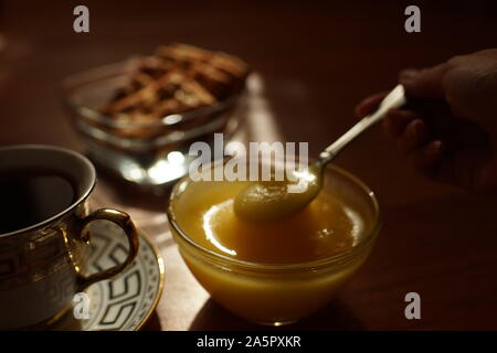 Tea Time. Honig in einem Glas Schale mit einem Löffel, eine Tasse Kaffee auf einer Untertasse, Cookies in einer Vase auf dem Tisch. Stockfoto