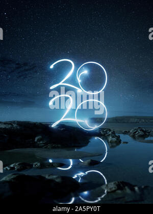Frohes Neues Jahr 2020 Lichteffekt schreiben in Wasser an einem Strand in der Nacht widerspiegelt. Lange Belichtung Landschaft Foto Composite. Stockfoto