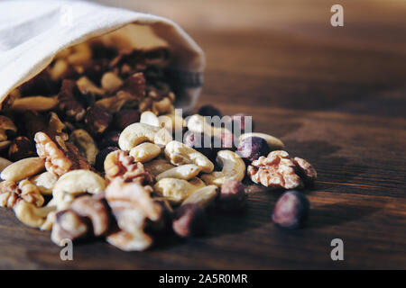 Mischung von Nüssen und Trockenfrüchten in sackleinen Beutel auf Holztisch, gesunde Speisen und Snacks - Konzept, kopieren Platz für Text Stockfoto