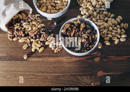 Auswahl der vielfältigen Schalenfrüchte und getrocknete Früchte in weißen Schalen und sackleinen Säcke auf einem Holztisch, gesunde Ernährung Konzept, kopieren Platz für Text Stockfoto