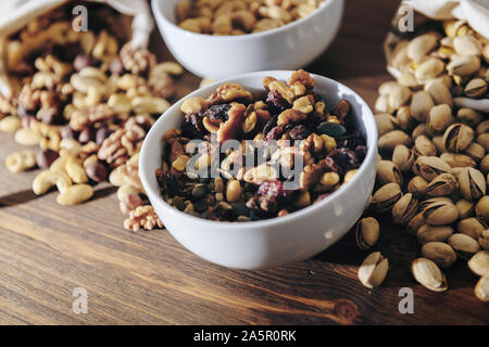 Weiße Schüssel mit gemischte Nüsse, Trockenfrüchte und Pistazien auf rustikalen Holztisch, gesunde Speisen und Snacks - Konzept, kopieren Platz für Text Stockfoto