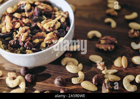 Weiße Schüssel mit gemischten Nüssen auf rustikalen Holztisch, gesunde Speisen und Snacks - Konzept Stockfoto