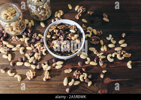 Blick von oben auf eine weiße Schale mit abwechslungsreichen Bio Trockenfrüchte und Gläser mit gemischten Nüssen auf rustikalen Holztisch, gesunde Speisen und Snacks - Konzept Stockfoto
