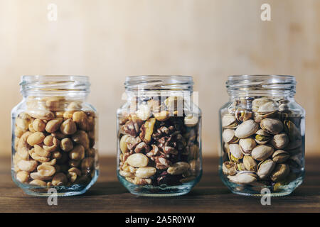 Drei Gläser mit gemischten Nüssen und Trockenfrüchten innen auf einem rustikalen Holztisch, gesunde Speisen und Snacks - Konzept, kopieren Platz für Text Stockfoto