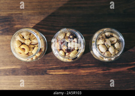 Blick von oben auf die drei Gläser mit gemischten Nüssen und Trockenfrüchten innen auf einem rustikalen Holztisch, gesunde Speisen und Snacks - Konzept, kopieren Platz für Text Stockfoto