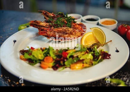 Gebratene Garnelen in Knoblauch Sauce serviert, in der Schale, mit frischem Salat und Zitrone Stockfoto