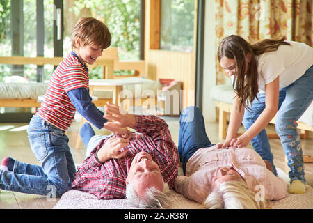 Großeltern auf dem Boden sind von ihren Enkelkindern tickled Stockfoto