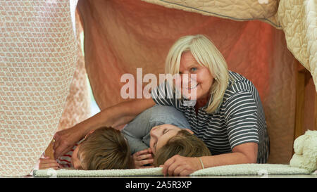 Glückliche Oma mit zwei Enkelkinder Kinder schlafen unter Decke wie ein Zelt Stockfoto